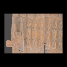 Dwuczęściowe połączone żelaznymi klamrami drewniane drzwiczki do spichlerza ludu Dogon z Mali. Na zewnętrznej stronie trzy rzędy płaskorzeźbionych postaci i schematyczne popiersia. W środku lewego brzegu drewniany zamek zasuwkowy.